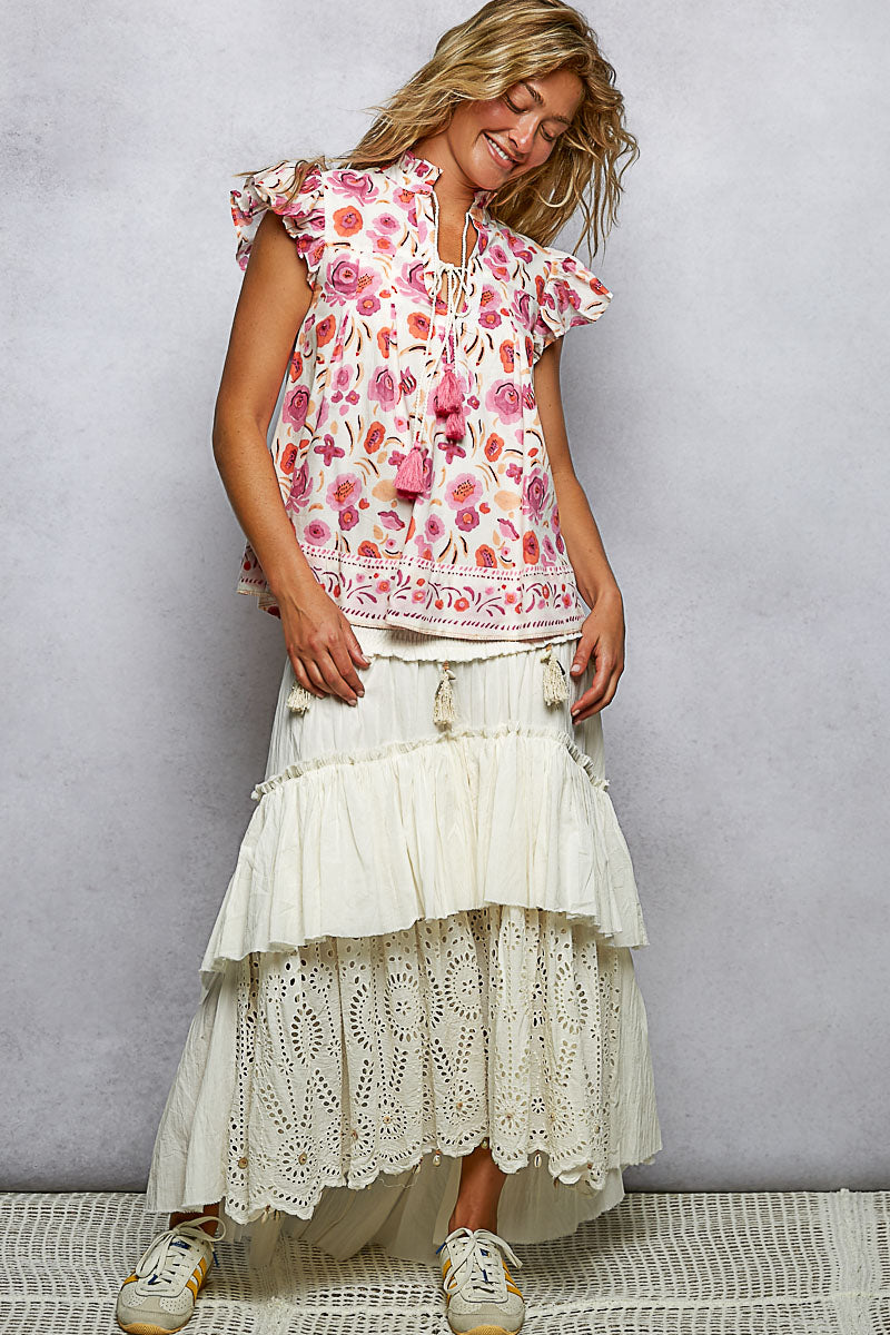 Woman wearing a floral top and white lace skirt against a plain background