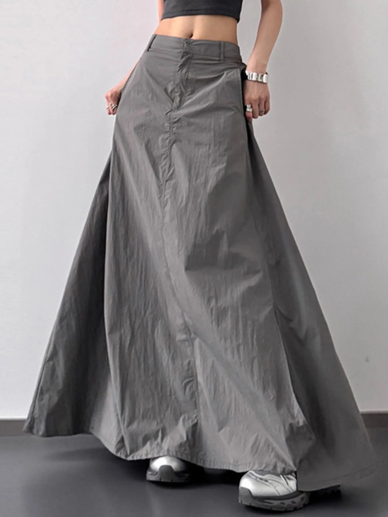 Person wearing a long gray skirt on a plain background
