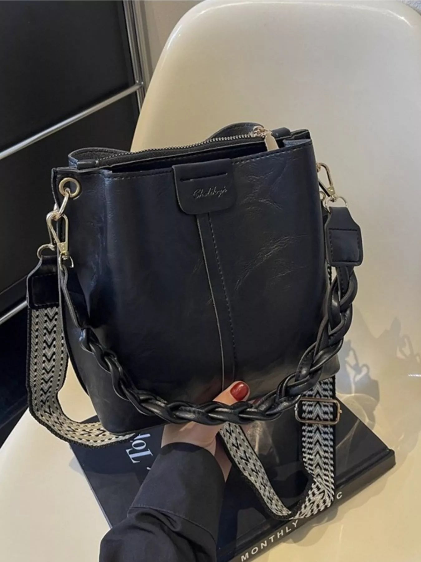 Black handbag with a chain strap held by a person on a white surface.