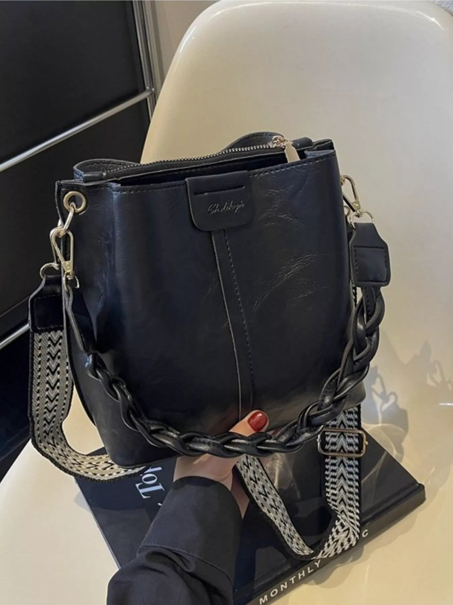 Black handbag with a chain strap held by a person on a white surface.