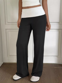 Person wearing black wide-leg pants and a white top against a neutral wall.