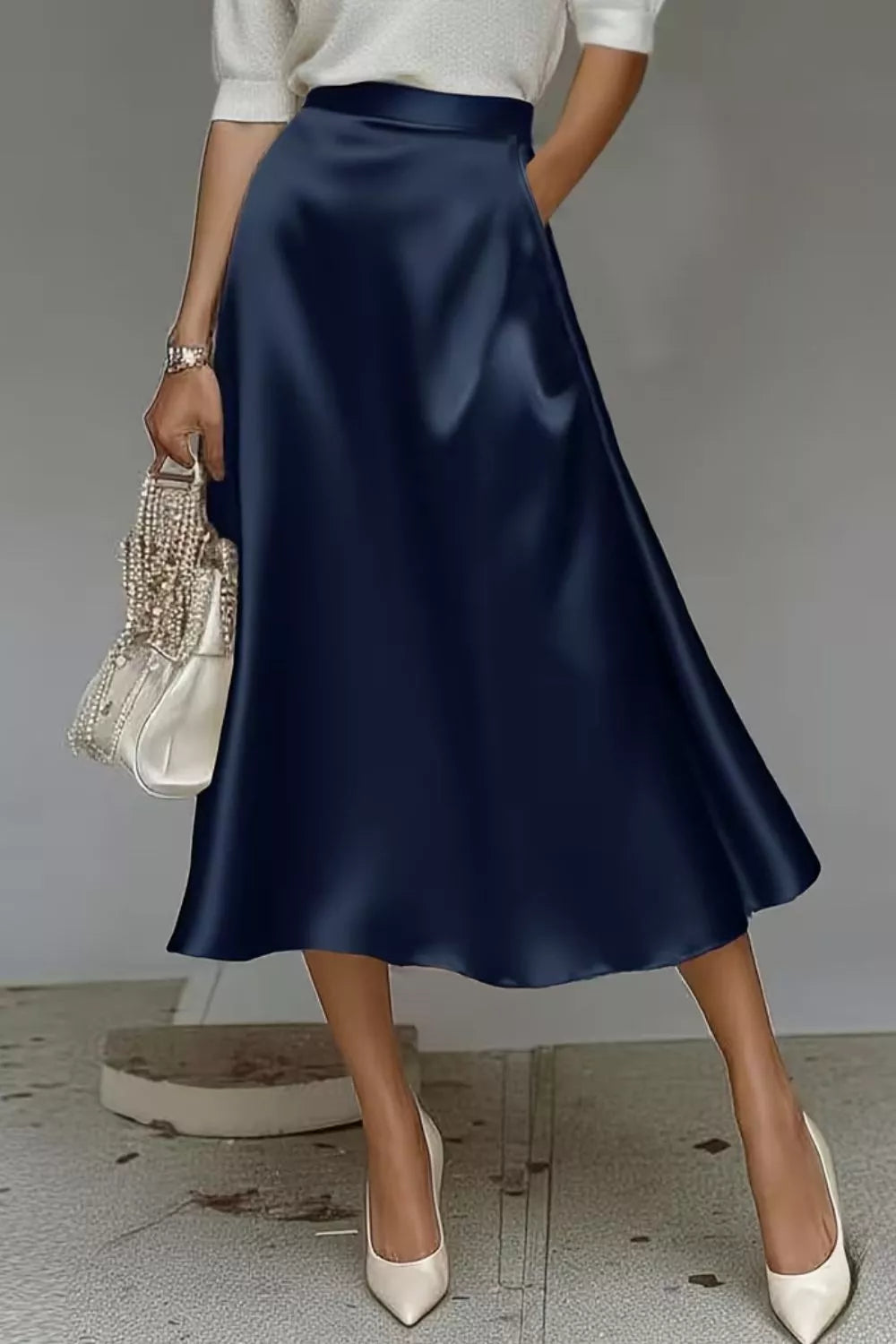 Person wearing a navy blue satin skirt with a white top and shoes, holding a small handbag.