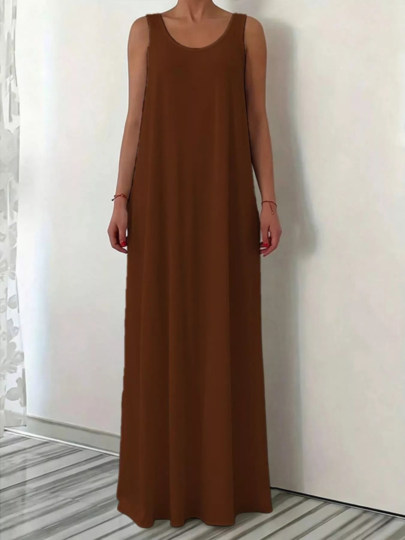 Brown sleeveless dress worn by a person against a white wall.