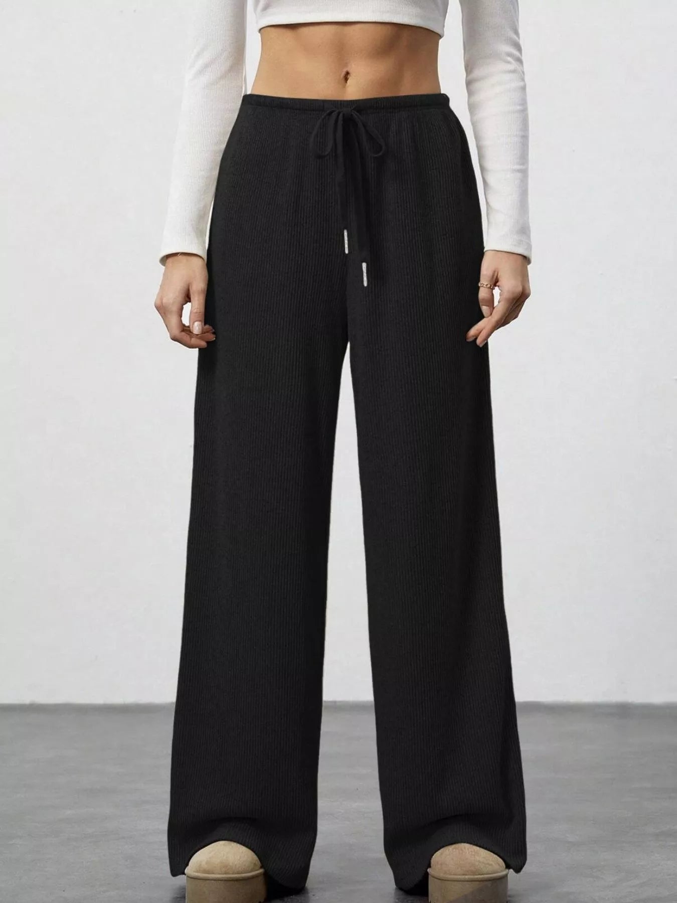Person wearing black wide-leg pants with a white top on a plain background