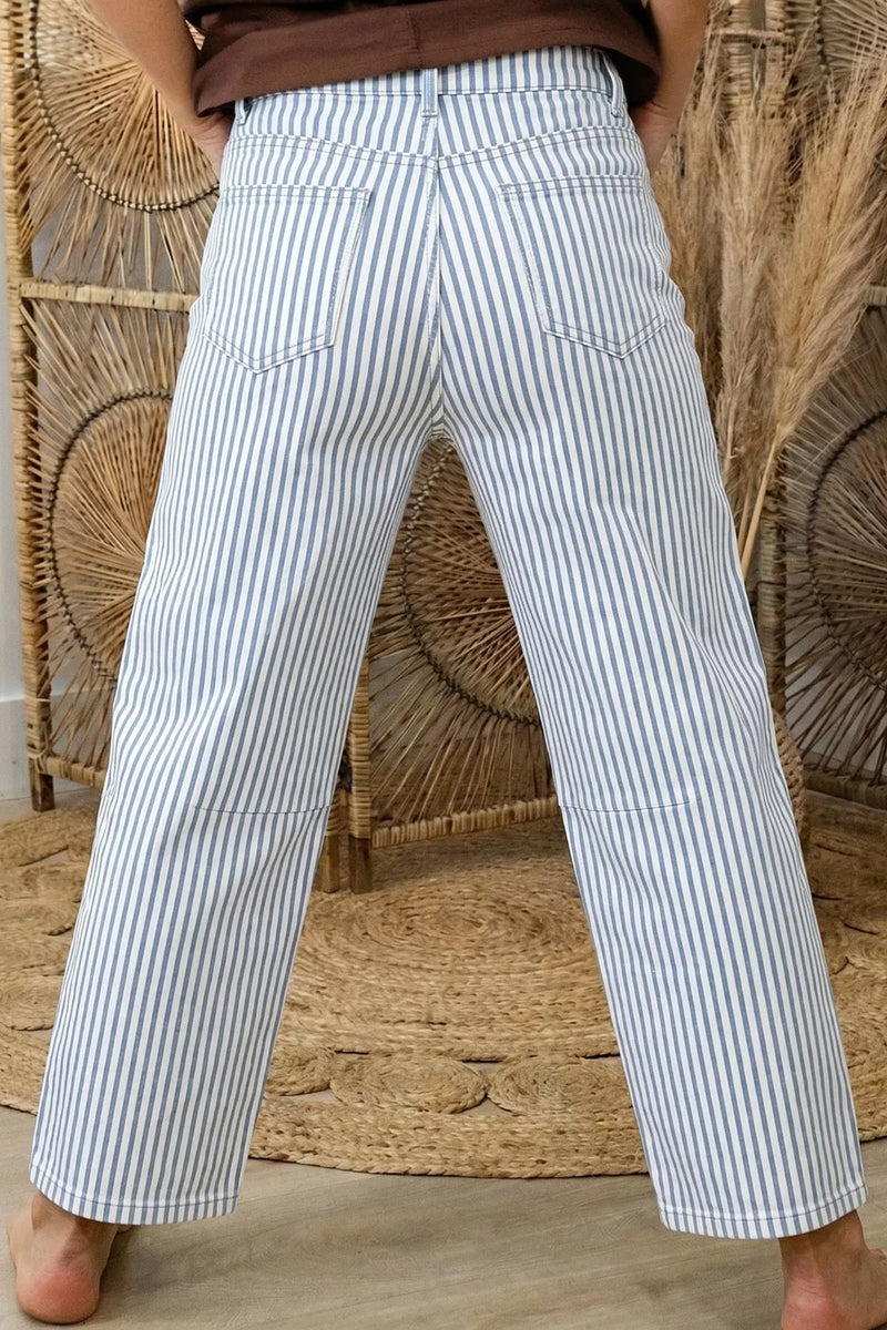 Person wearing white and blue striped pants standing against a woven wall.