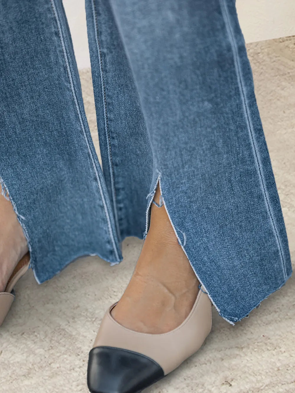 Close-up of blue jeans with a hem and beige shoes on a light background