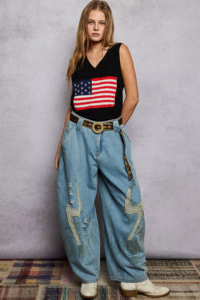 Person wearing a black tank top with an American flag design and blue jeans against a gray background