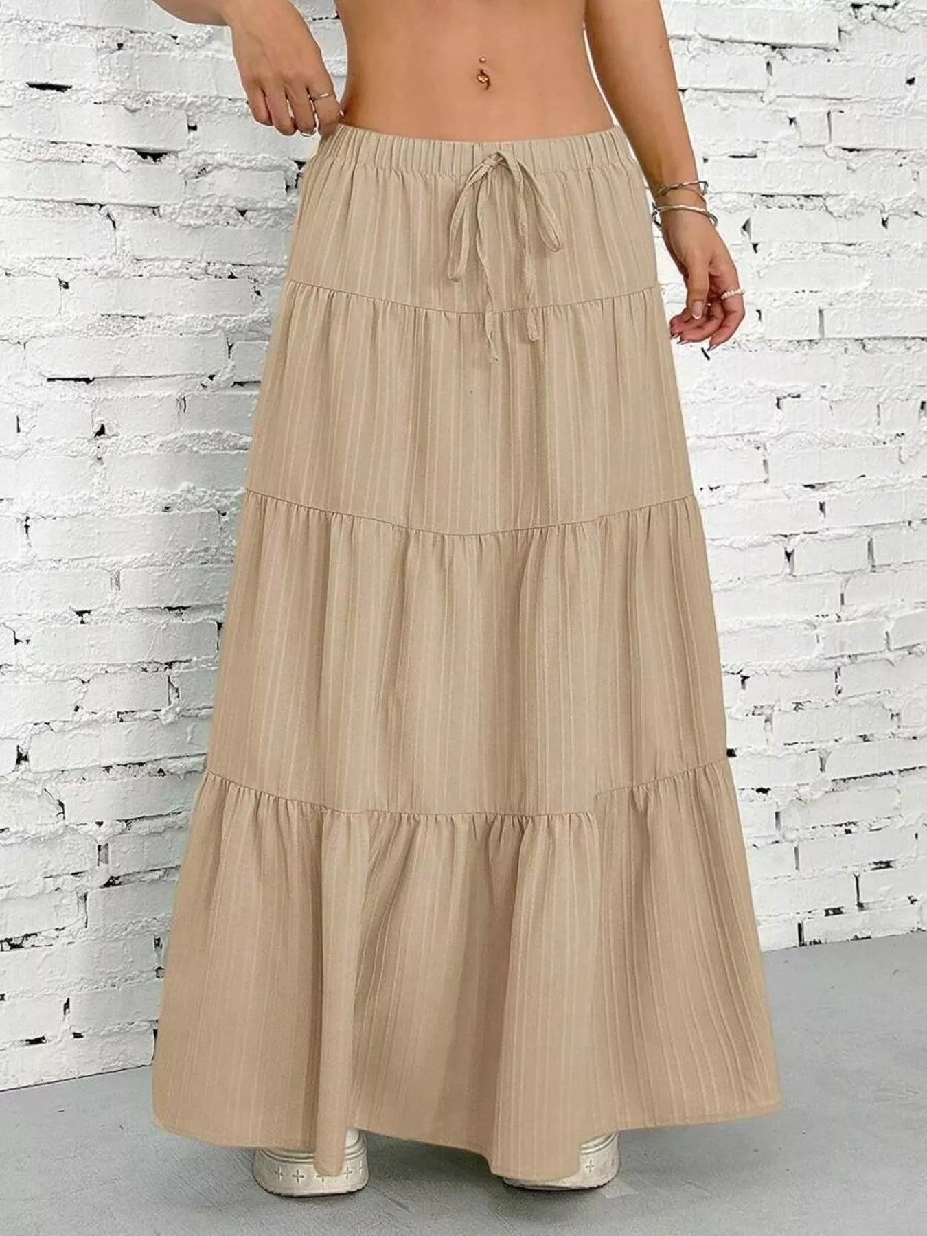 Beige tiered skirt worn by a person against a white brick wall.