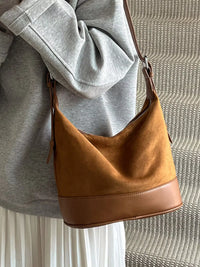 Brown leather handbag held by a person wearing a gray sweatshirt and white pants.