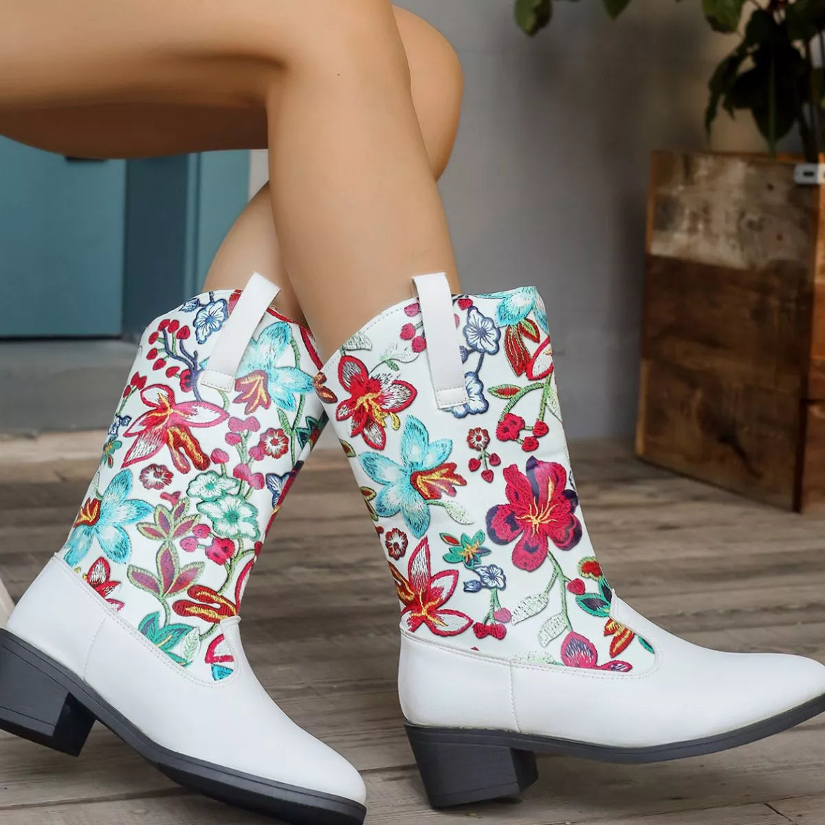 White boots with colorful floral patterns worn by a person sitting on a wooden floor.