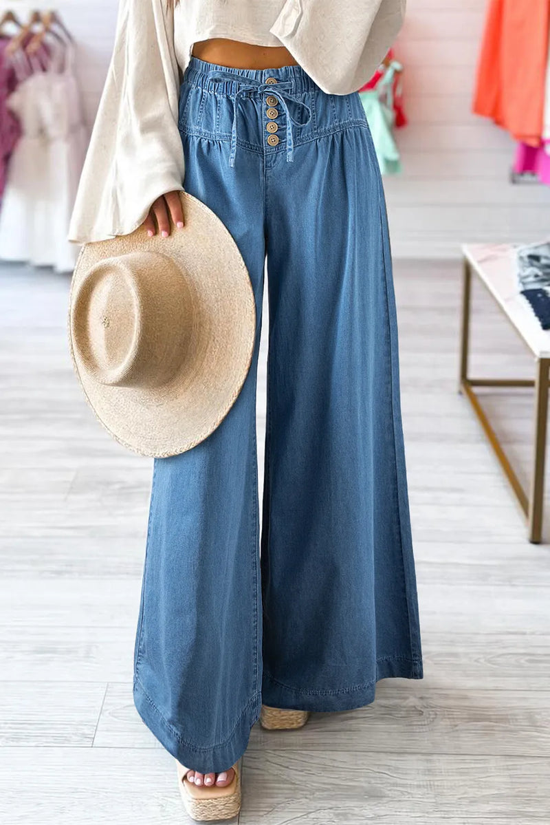 Person wearing blue wide-leg pants holding a straw hat in a store setting
