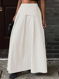 Person wearing a white skirt standing against a brick wall.