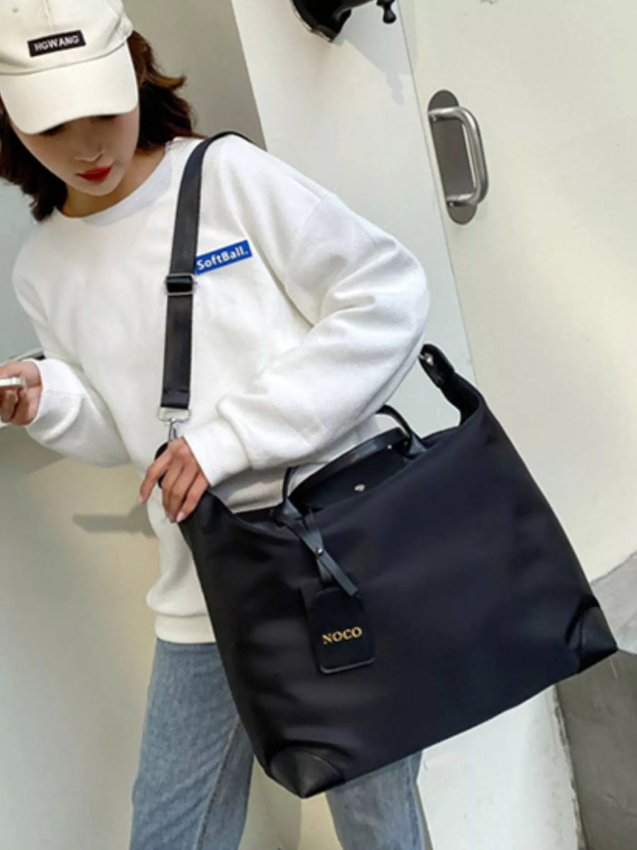 Person holding a black bag with visible branding, wearing a white sweatshirt and cap.