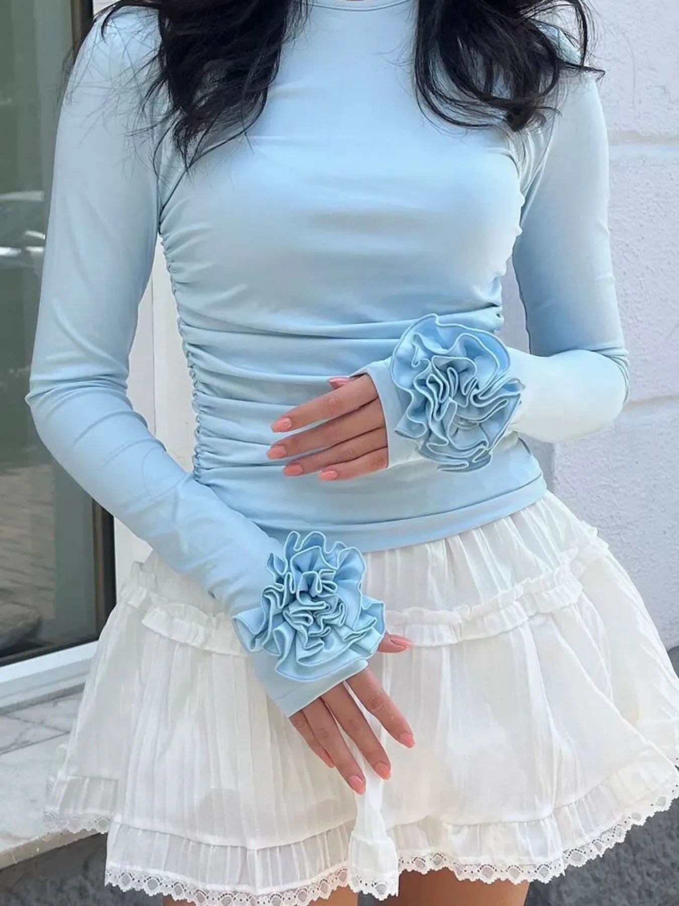 Person wearing a light blue long-sleeve top and matching gloves with floral details, standing against a neutral background.