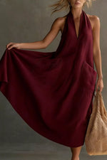 Woman wearing a burgundy dress holding a beige bag against a neutral background