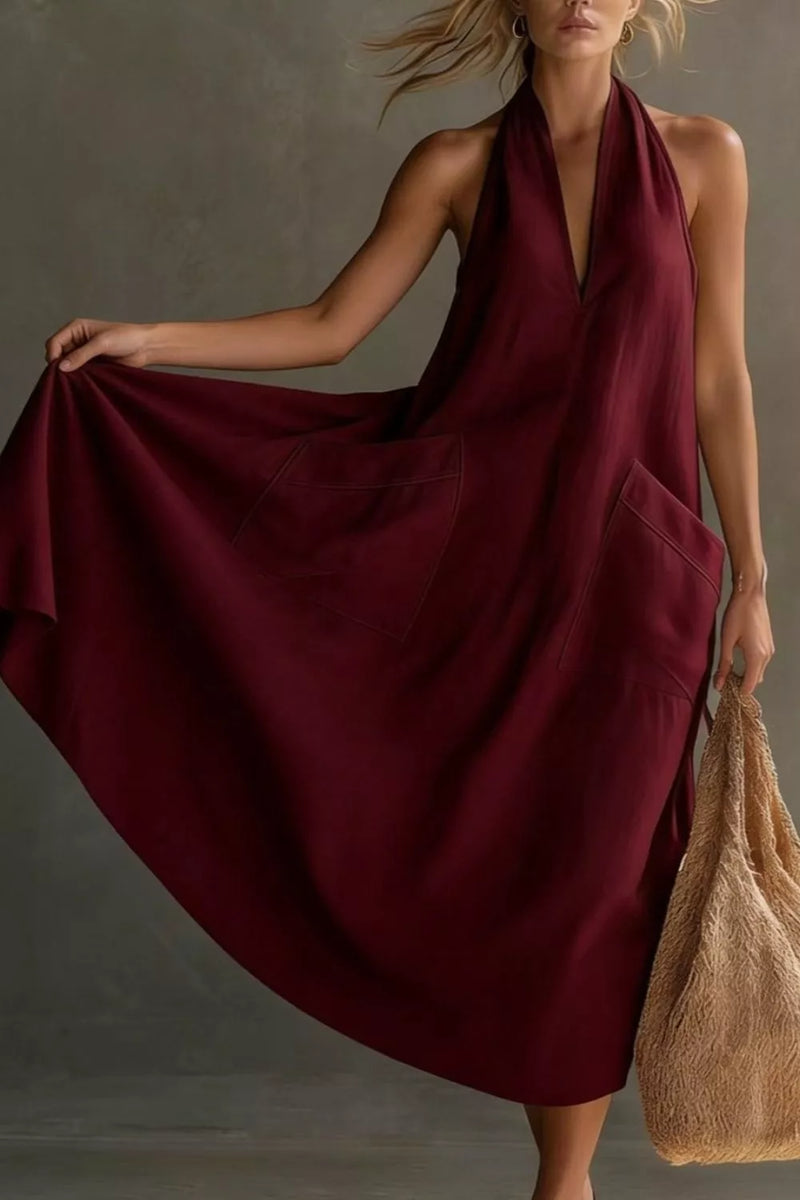 Woman wearing a burgundy dress holding a beige bag against a neutral background