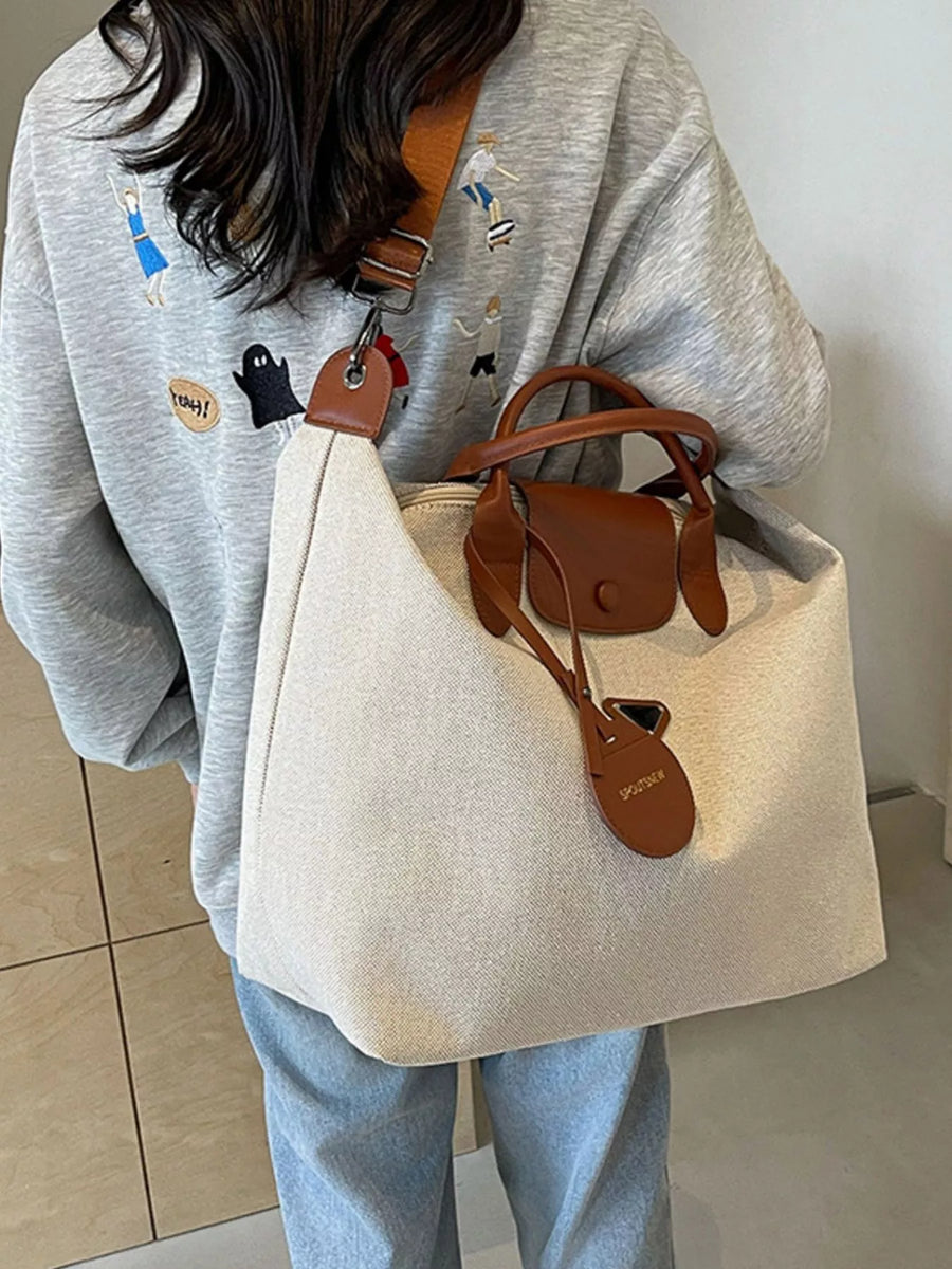 Person holding a beige tote bag with brown leather straps against a neutral background