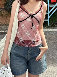 Person wearing a pink plaid top with black trim and denim shorts outdoors.