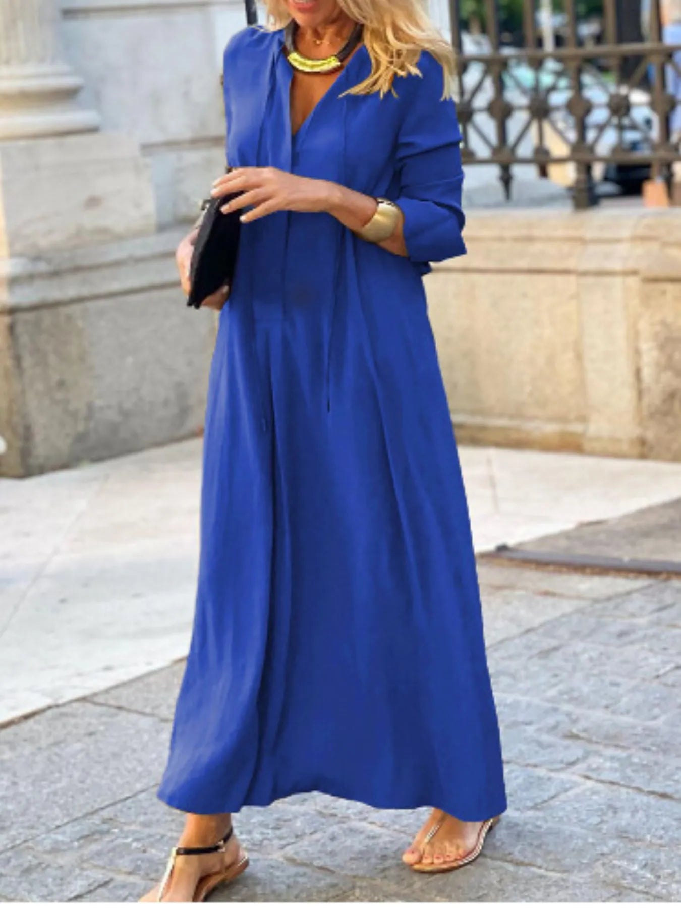Woman wearing a blue dress holding a black clutch in an urban setting.