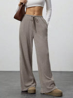 Person wearing brown wide-leg pants with a white top against a plain background