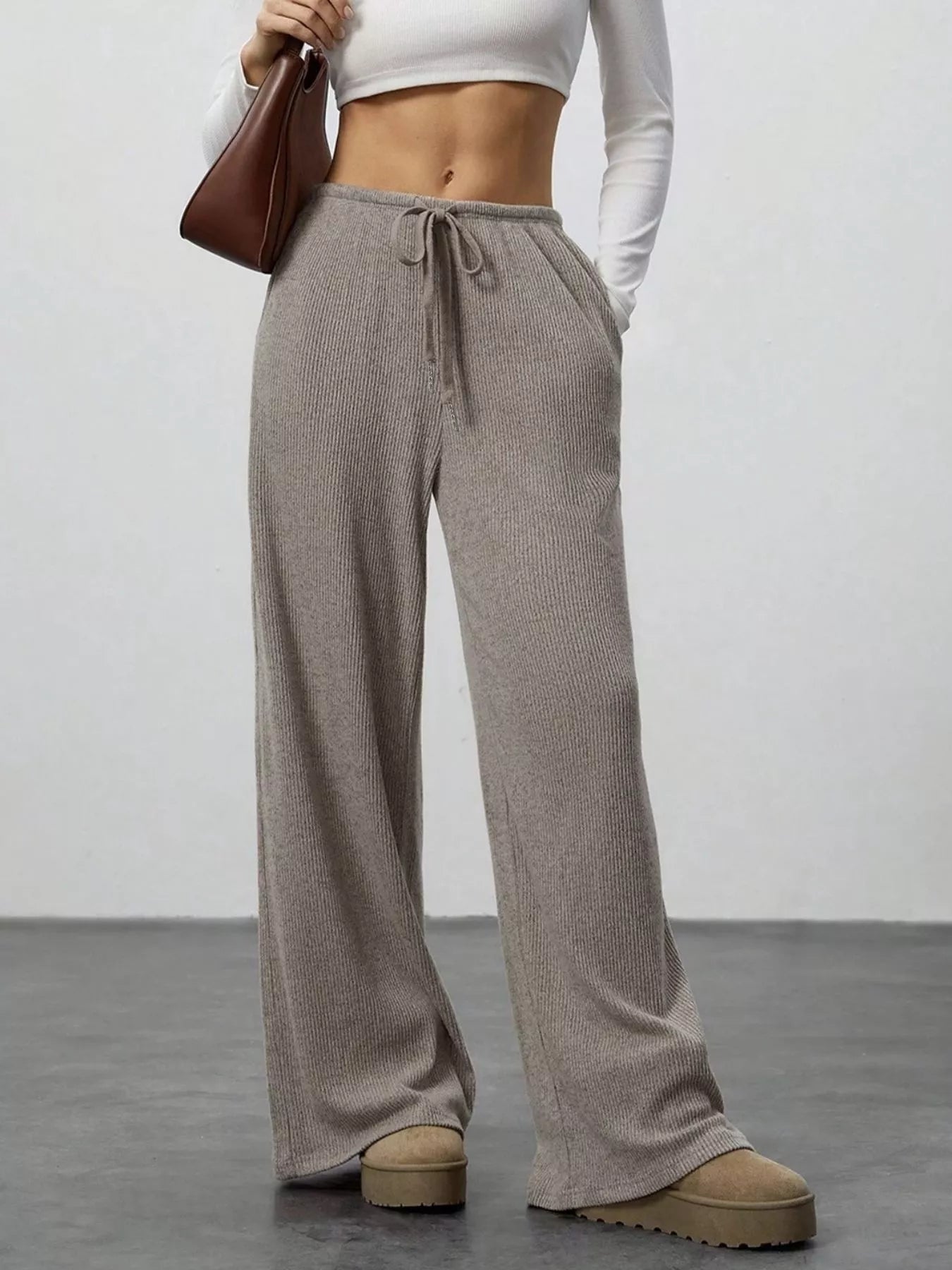 Person wearing brown wide-leg pants with a white top against a plain background