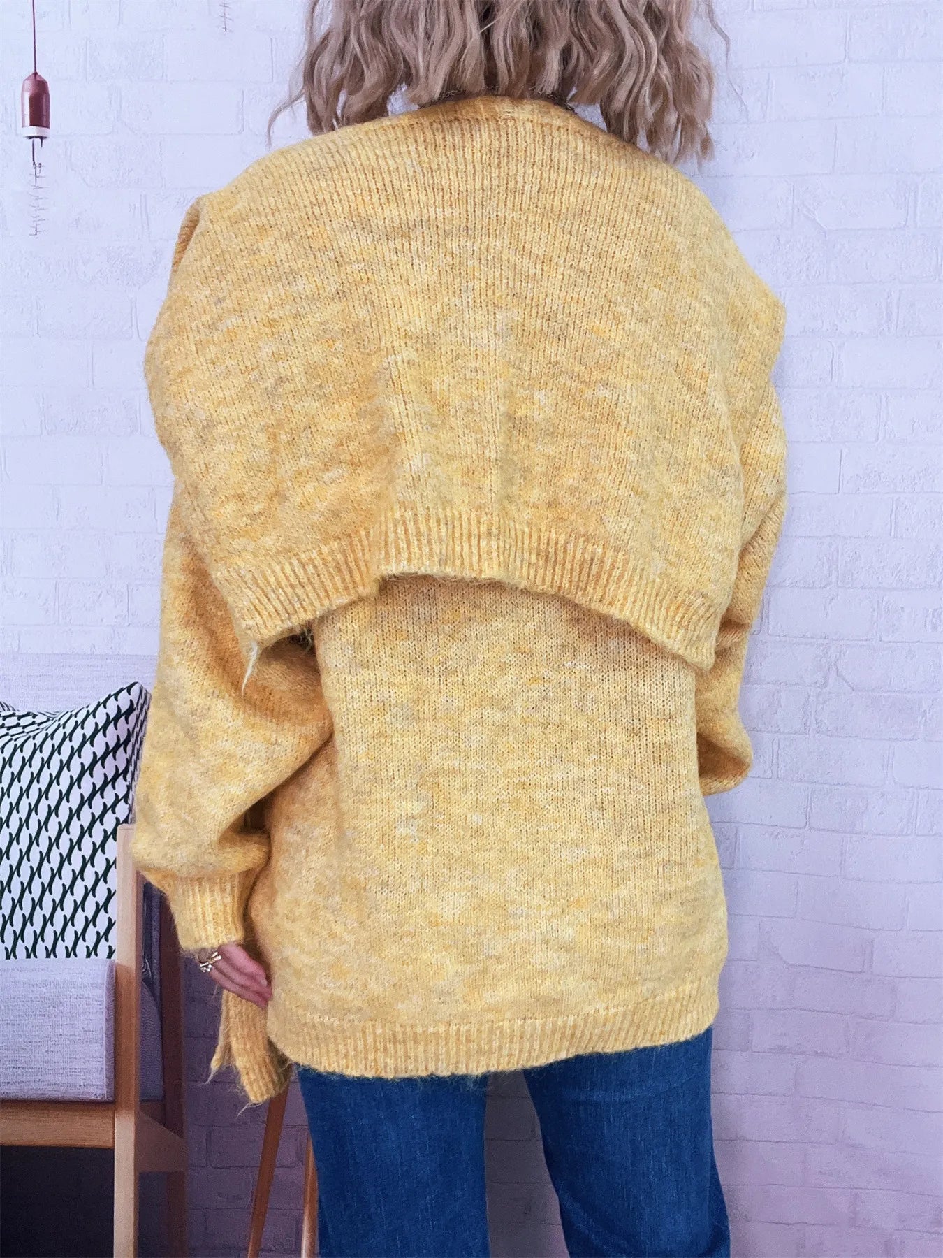 Person wearing a yellow knitted sweater with a white brick wall background