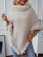 Woman wearing a beige knitted poncho with fur trim indoors.