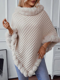 Woman wearing a beige knitted poncho with fur trim indoors.