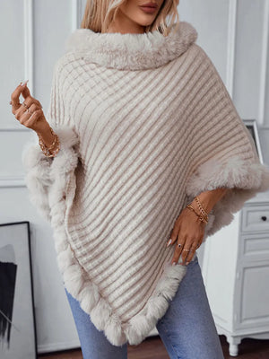 Woman wearing a beige knitted poncho with fur trim indoors.