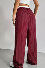 A person wearing high-waisted, wide-leg trousers in burgundy with thin white vertical pinstripes, shown from the back against a light gray wall and floor.