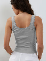 Woman wearing a gray tank top with lace trim on a plain background