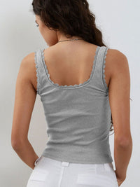 Woman wearing a gray tank top with lace trim on a plain background