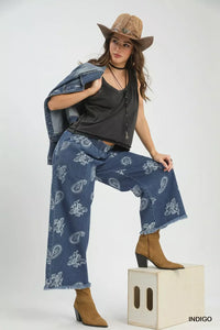 Woman wearing a black top, blue paisley pants, and brown cowboy hat on a white background