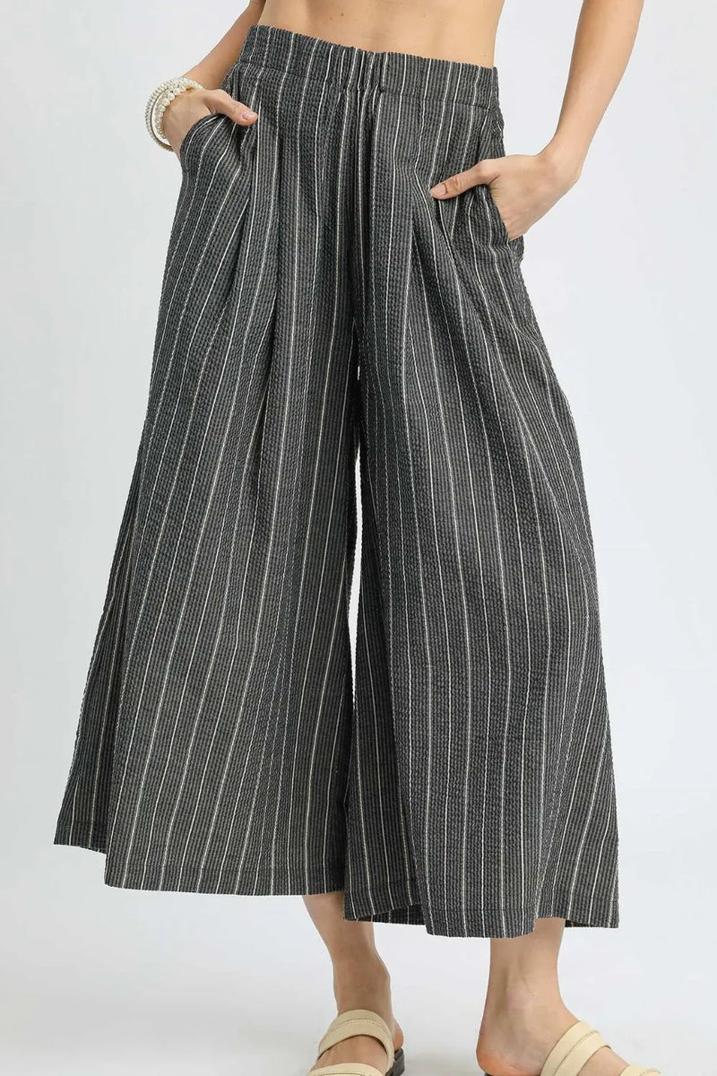Person wearing black and white striped wide-leg pants on a plain background