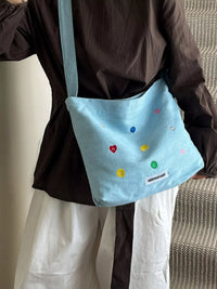 Person holding a light blue bag with colorful embellishments against a neutral background