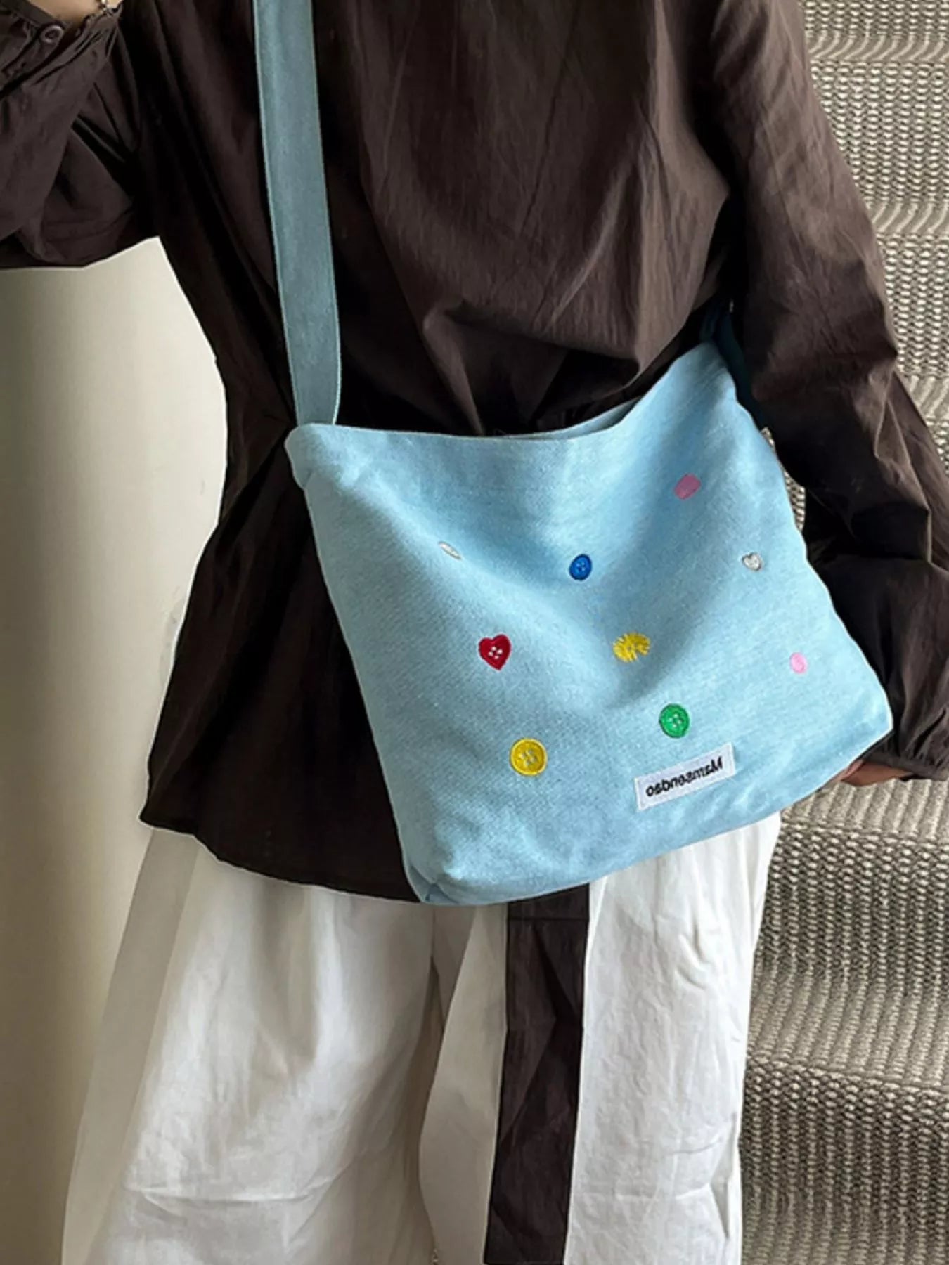 Person holding a light blue bag with colorful embellishments against a neutral background