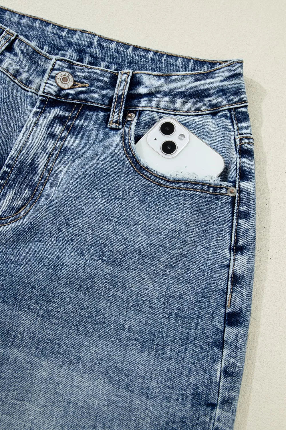 Close-up of blue denim jeans with a phone in the pocket on a beige background