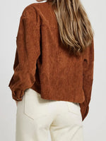 Person wearing a brown corduroy shirt and white pants on a plain background
