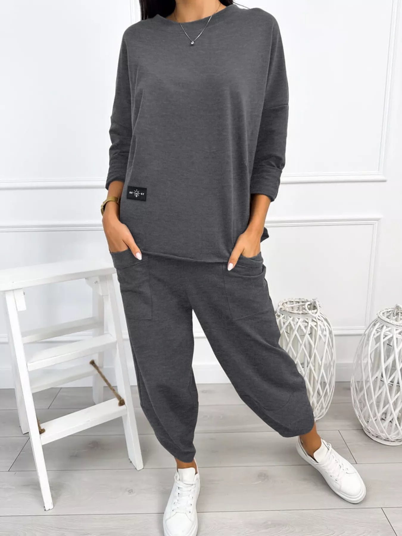 Person wearing a gray sweatshirt and pants set with white sneakers in a minimalistic room.