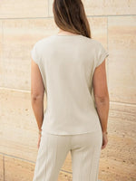 Woman wearing a light-colored sleeveless top and pants against a beige stone wall.