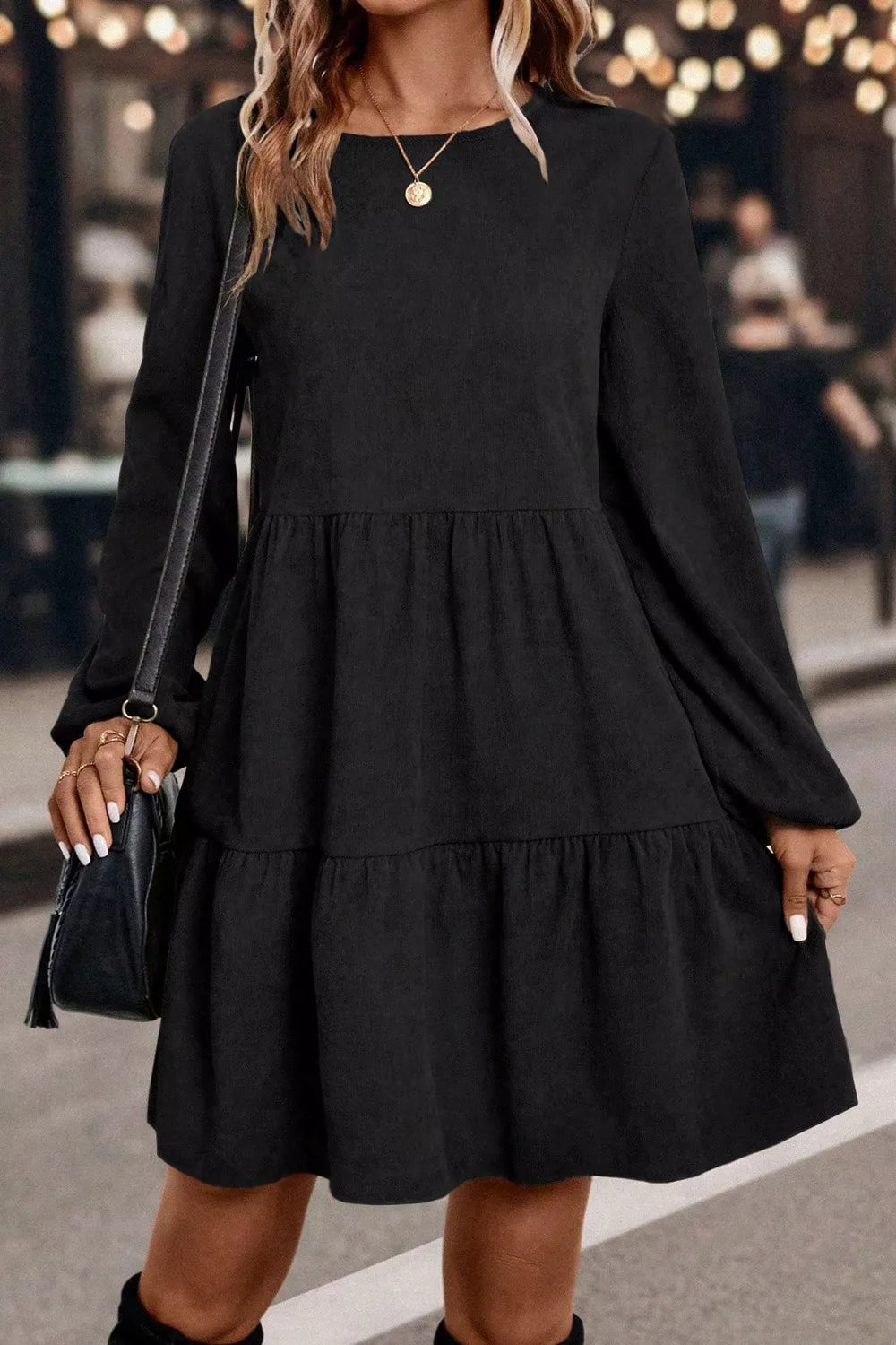 Woman wearing a black dress with long sleeves and layered skirt, holding a black handbag.
