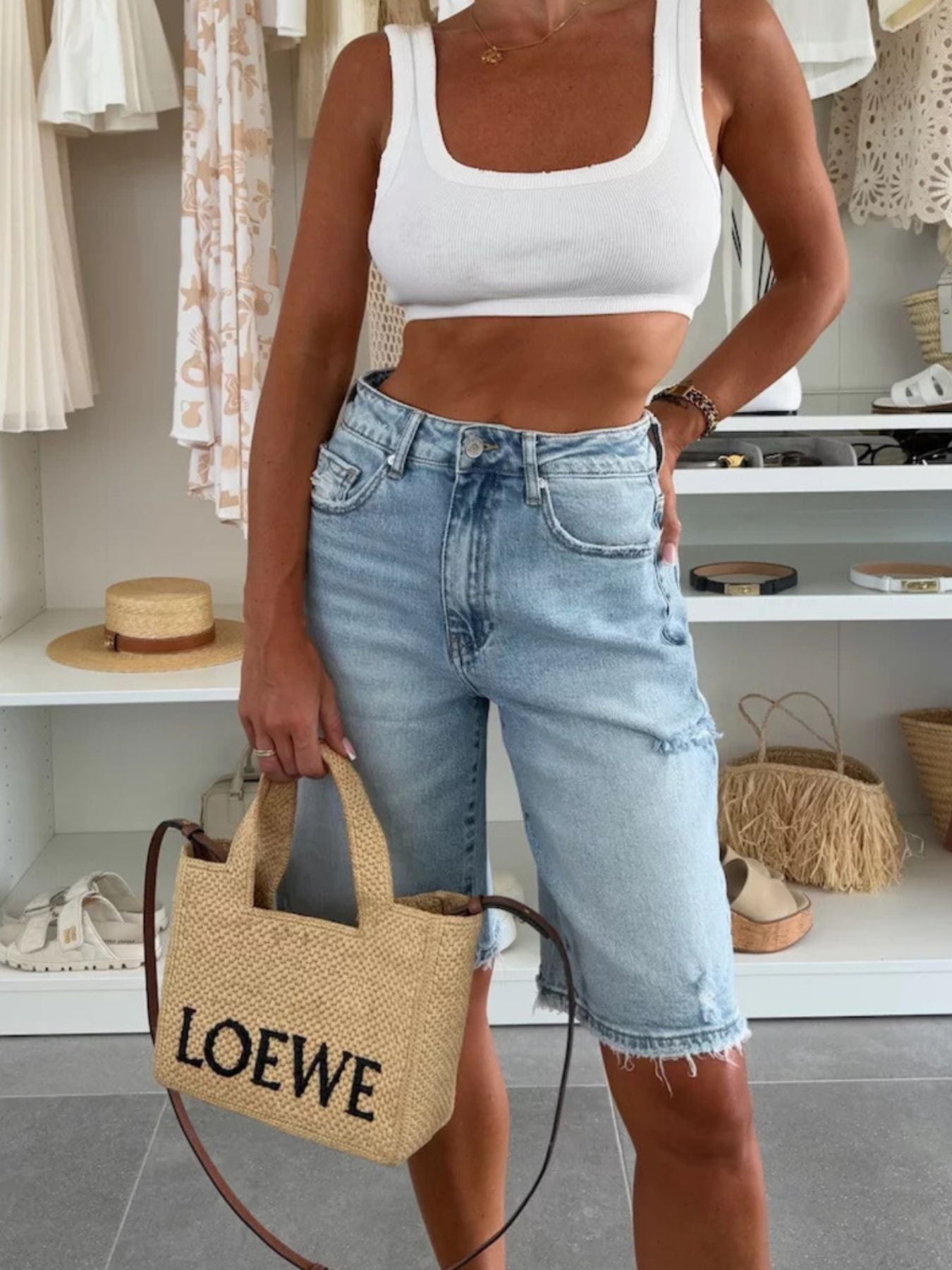 Person wearing a white crop top and light blue jeans, holding a Loewe bag in a store setting.