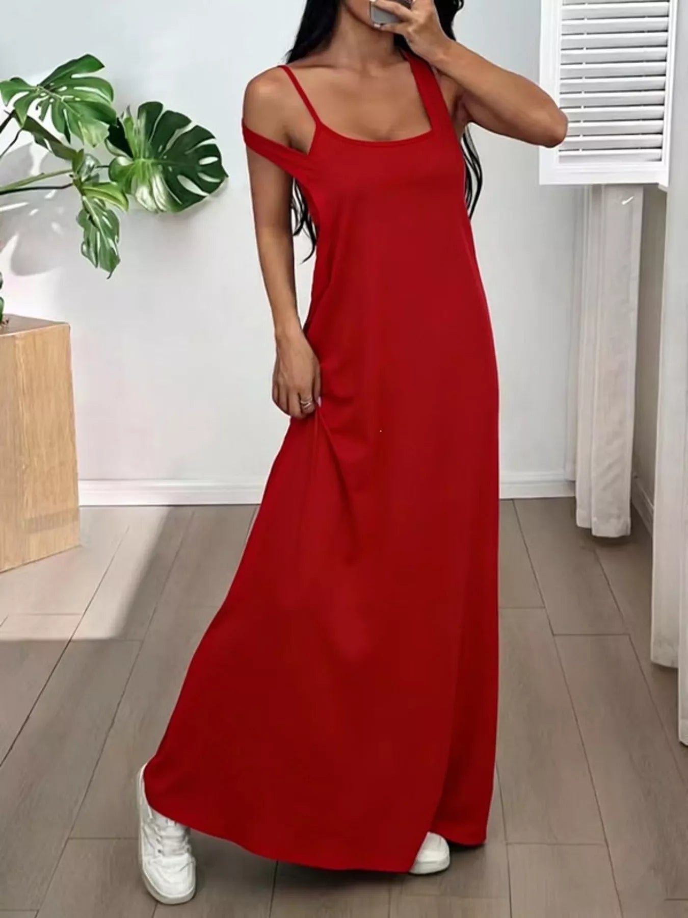 Woman wearing a red dress standing indoors with a plant and white door in the background
