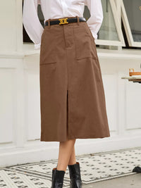 Person wearing a brown skirt with a white shirt and black belt outdoors.