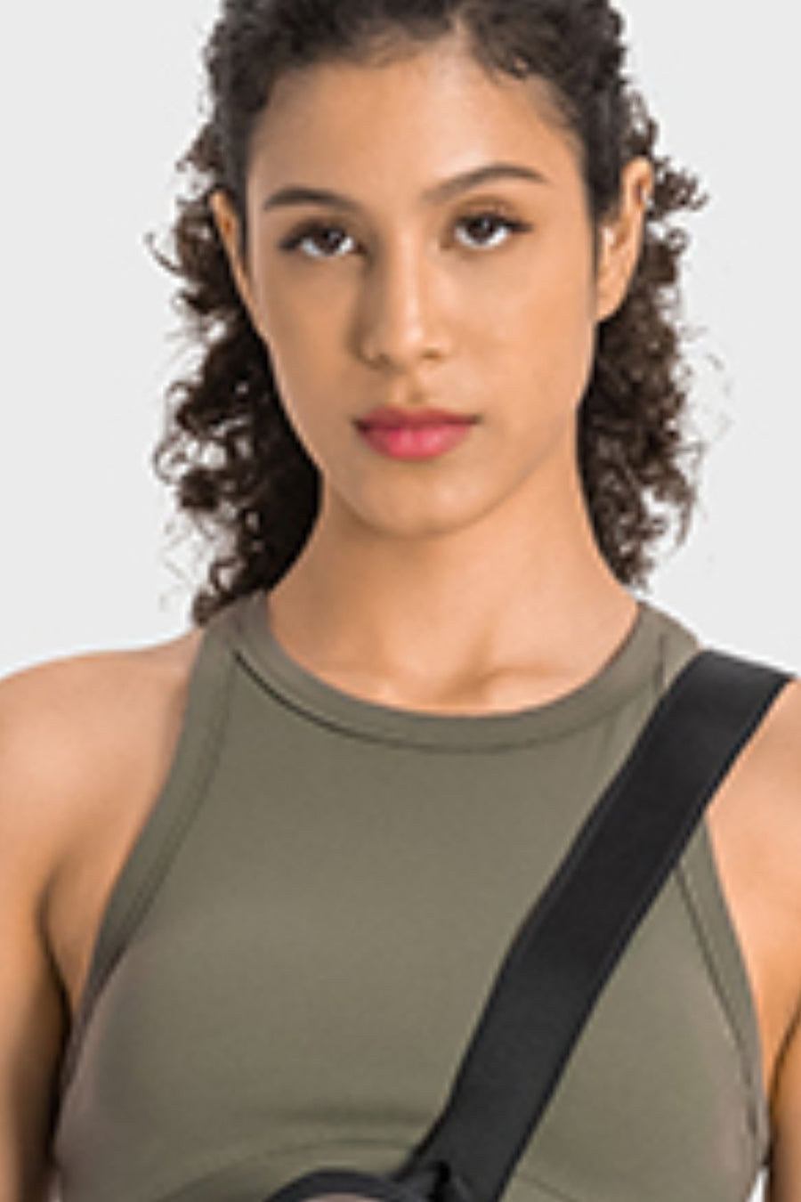 Woman wearing a green tank top with a black strap over her shoulder on a white background