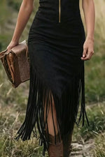 Person wearing a black fringe dress holding a brown leather bag in a natural setting.
