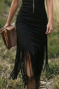 Person wearing a black fringe dress holding a brown leather bag in a natural setting.