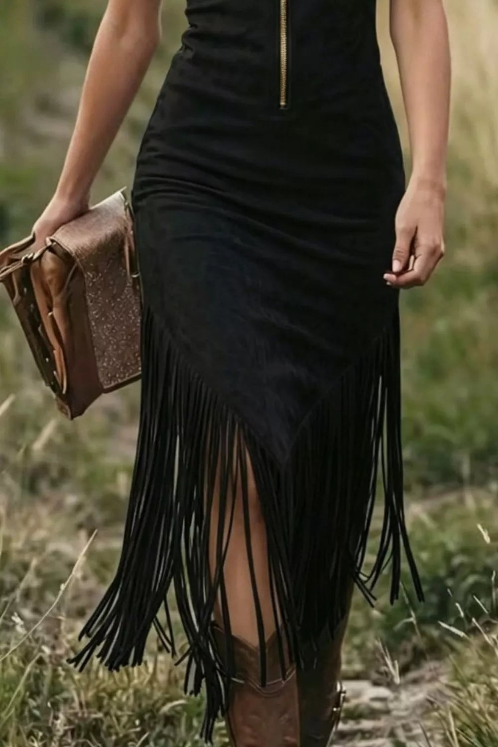 Person wearing a black fringe dress holding a brown leather bag in a natural setting.