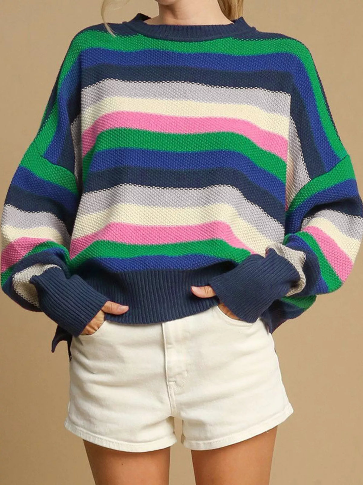 Person wearing a colorful striped sweater and white shorts on a beige background