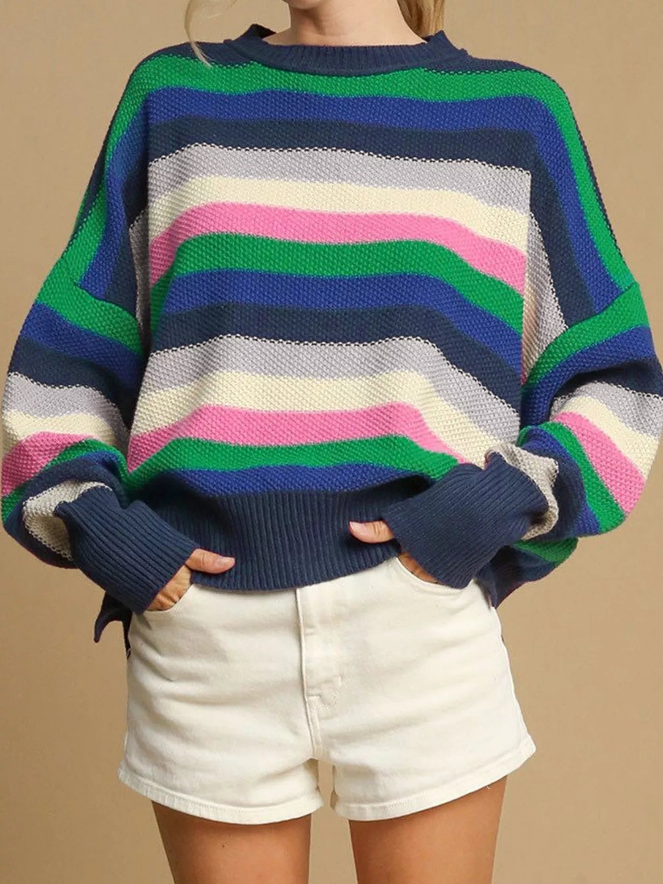 Person wearing a colorful striped sweater and white shorts on a beige background